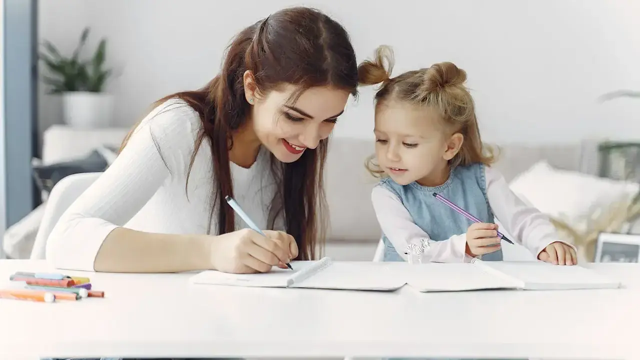 Mama uczy córkę odejmowania do 10. Dziewczynki piszą w zeszytach, a obok leżą kolorowe flamastry.
