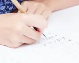 Dłonie ćwiczą pisanie liter, tworząc na papierze **duże l** i inne znaki.