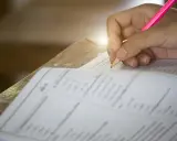 Dłoń pisząca ołówkiem po karcie testowej z zaznaczonymi odpowiedziami.