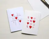 Ręcznie robione pomysły na kartki walentynkowe: gra w kółko i krzyżyk z serduszkami oraz kartka z serduszkami tworzącymi napis LOVE.
