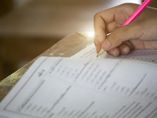 Dłoń pisząca ołówkiem po karcie testowej z zaznaczonymi odpowiedziami.