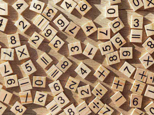 Drewniane kafelki z cyframi i symbolami matematycznymi, jakby ktoś uczył się dzielenia w słupku.