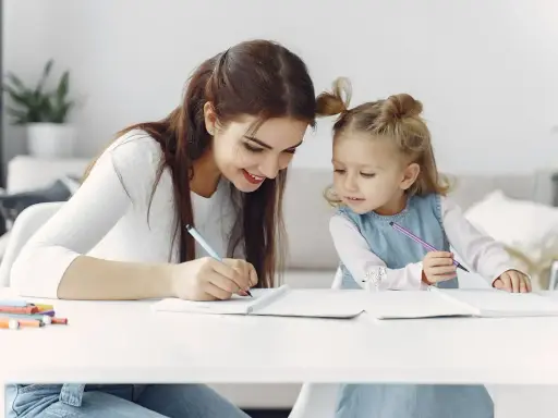 Mama uczy córkę odejmowania do 10. Dziewczynki piszą w zeszytach, a obok leżą kolorowe flamastry.