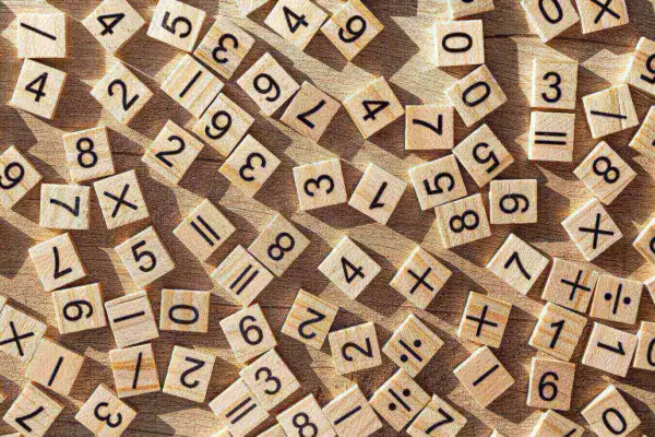Drewniane kafelki z cyframi i symbolami matematycznymi, jakby ktoś uczył się dzielenia w słupku.